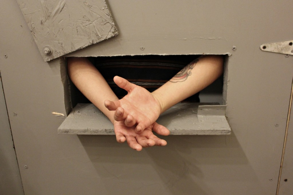 A young organizer poses with his hands extended through the model cell door's opening, as a prisoner would have to in order to be handcuffed before exiting the cell. (Photo: Kelly Hayes)